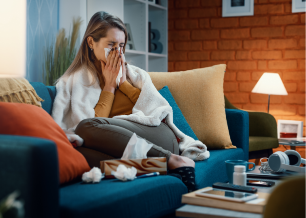 Sieviete, sēžot uz dīvāna, aizsedz degunu ar salveti.